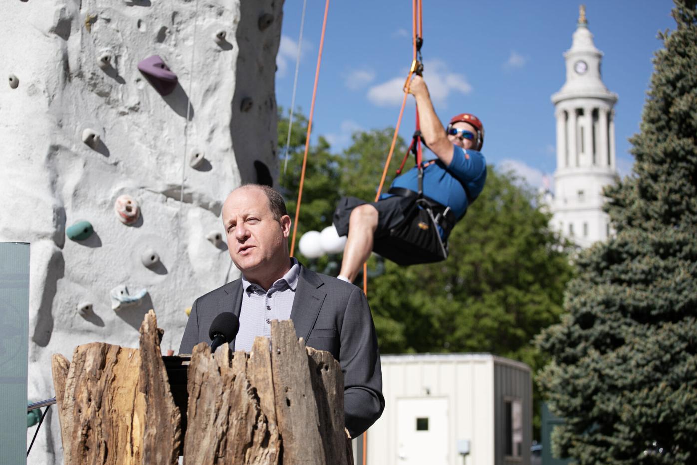 Gov. Jared Polis speaks while Gary Verrazano, an adaptive rock climber